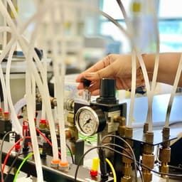 A picture of a hand adjusting a valve on a reactor with a lot of plastic tubing connections